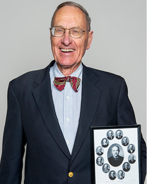 Frederick Lovejoy is holding a framed photograph of several men. 