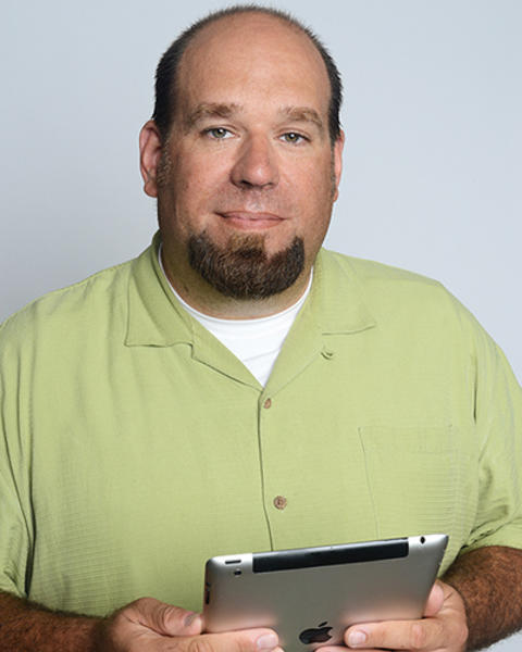 Mason Miranda is holding an iPad. He is wearing a light green shortsleeve button down shirt.