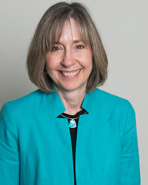 Jane Neill is wearing a turquoise jacket, turquoise necklace, and black shirt.
