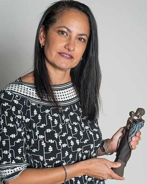 Nawal Nour is wearing a black and white patterned dress and holding a Maasai statue of a mother kissing her child