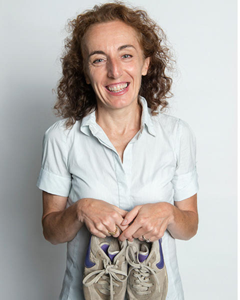 Simonetta Piergentili is holding up a battered pair of gray and purple sneakers.