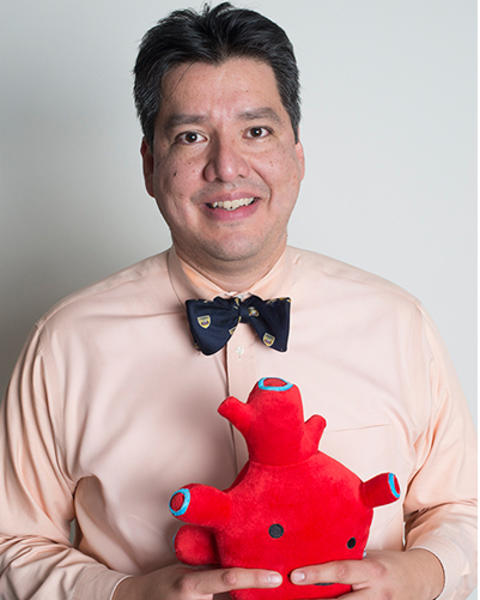 Fidencio Saldana is wearing a peach shirt and blue patterned bowtie. He is holding a cutesy heart plush.