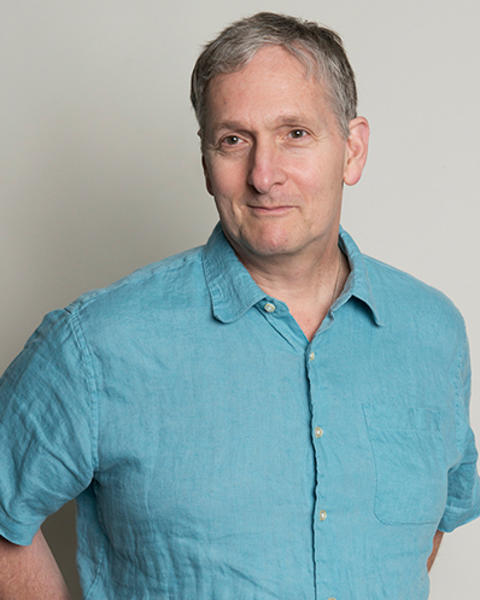Clifford Tabin is wearing a turquoise short sleeve button down shirt. He is facing slightly to the right of the camera.