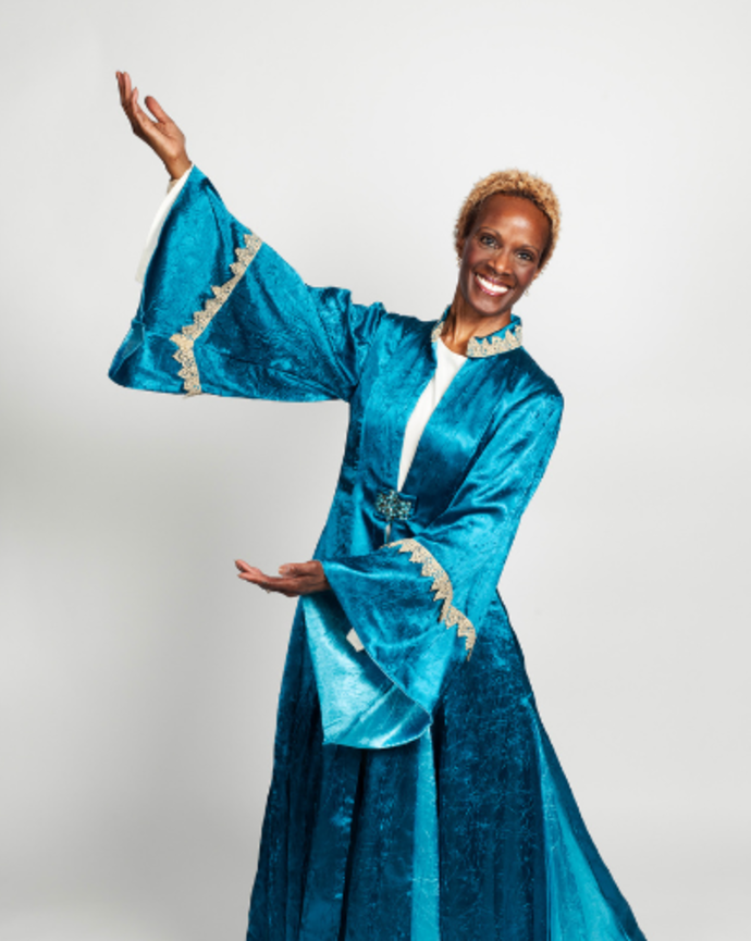 Teresa Carter is wearing a velvet blue gown. Her arms are extended to one side and one of her feet is pointed to the other side, in a gesture of movement.