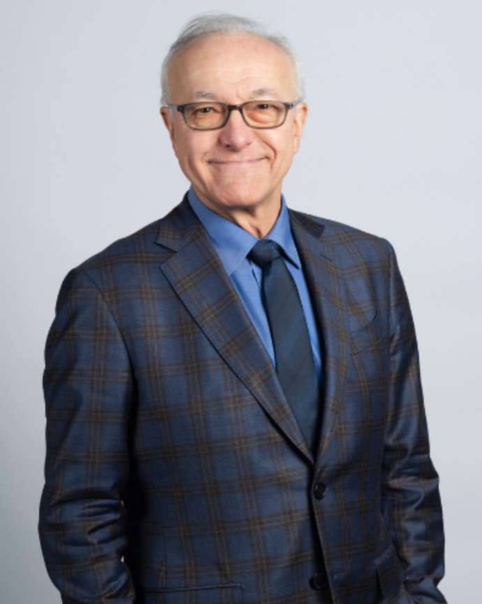 George Daley is wearing a plaid dark blue suit, blue shirt, and dark blue tie. He is casually standing with his hands in his pant pockets.