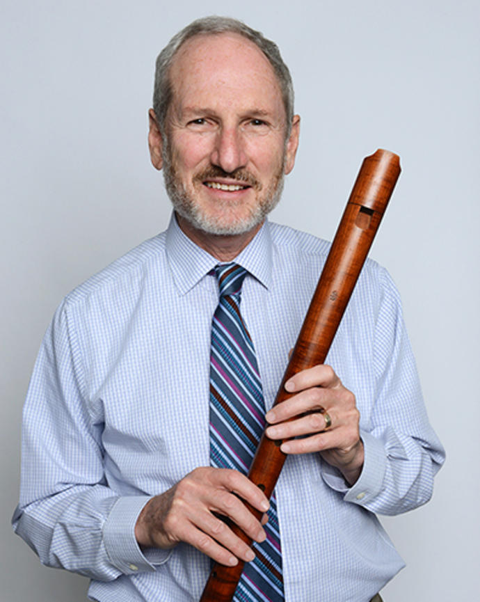 David Bor is holding a renaissance recorder which looks like a long wooden flute. 