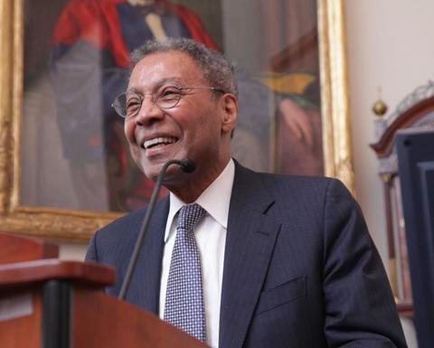 Alvin Poussaint smiles as he stands behind a lectern in the Waterhouse Room. 