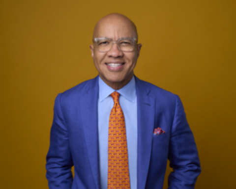 A waist-up photo of Darren Walker, smiling in a bright blue suit and orange tie. 