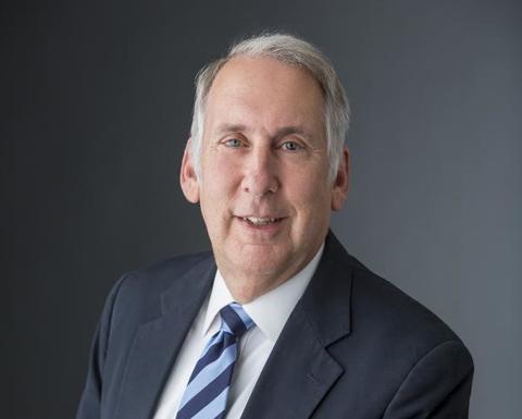 Edward Halperin is wearing a black blazer, white shirt, and blue striped tie.