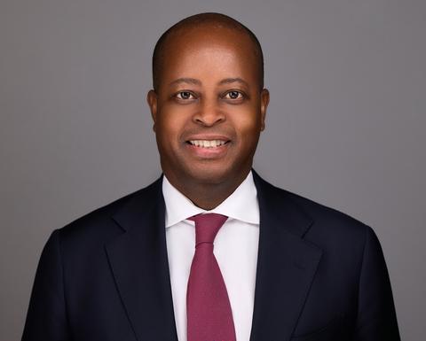 Wayne Frederick is wearing a maroon tie, white shirt, and black blazer. 