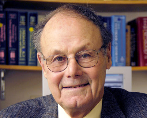 David Nathan sitting in front of a bookshelf. He is wearing a blue patterned blazer, yellow shirt, and red tie.