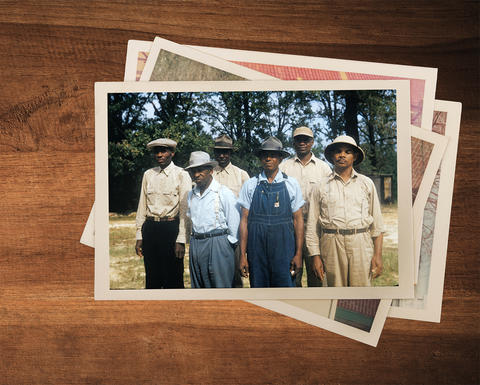 A photo of a group of Black men sits on a pile of more photos on a wooden surface.