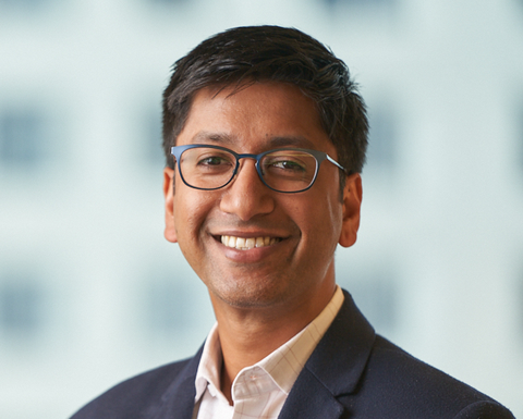 Guarav Singal is wearing a white shirt and black blazer. He has black-rimmed glasses and is smiling.