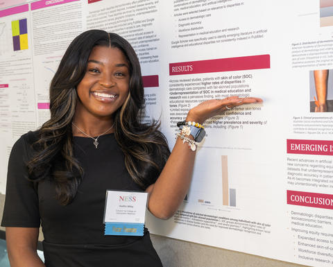 A NESS presenter gestures to her research poster she is standing in front of.