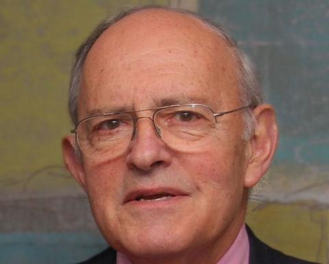 Mitchell Rabkin is a mostly bald man with gray hair and glasses. He is wearing a pink shirt, burgundy tie, and black blazer.